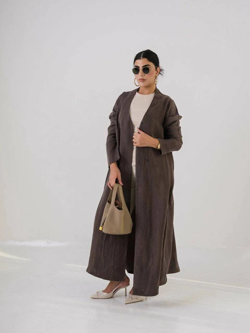 woman wearing luxurious brown abaya made of lightweight cobra silk with subtle sheen and fluid texture carrying beige handbag