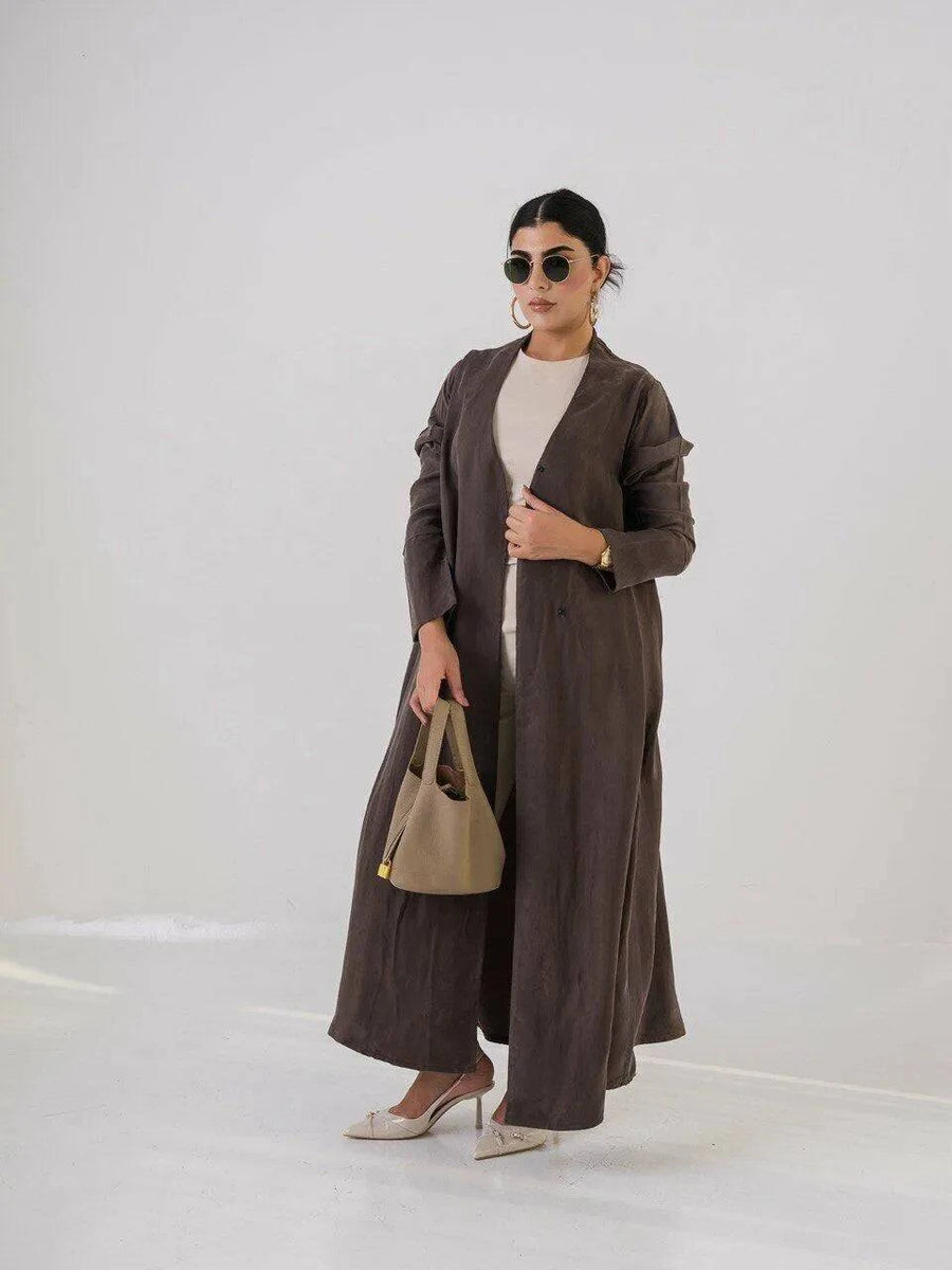 woman wearing luxurious brown abaya made of lightweight cobra silk with subtle sheen and fluid texture carrying beige handbag