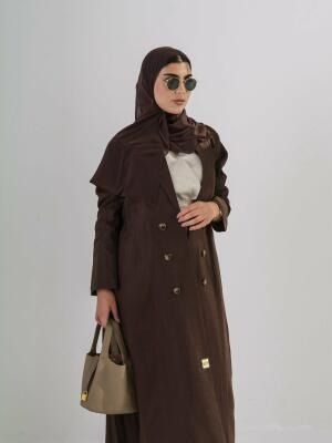 Woman wearing a brown crepe abaya with a structured silhouette and three buttons on each side, paired with a matching brown headscarf and beige handbag.