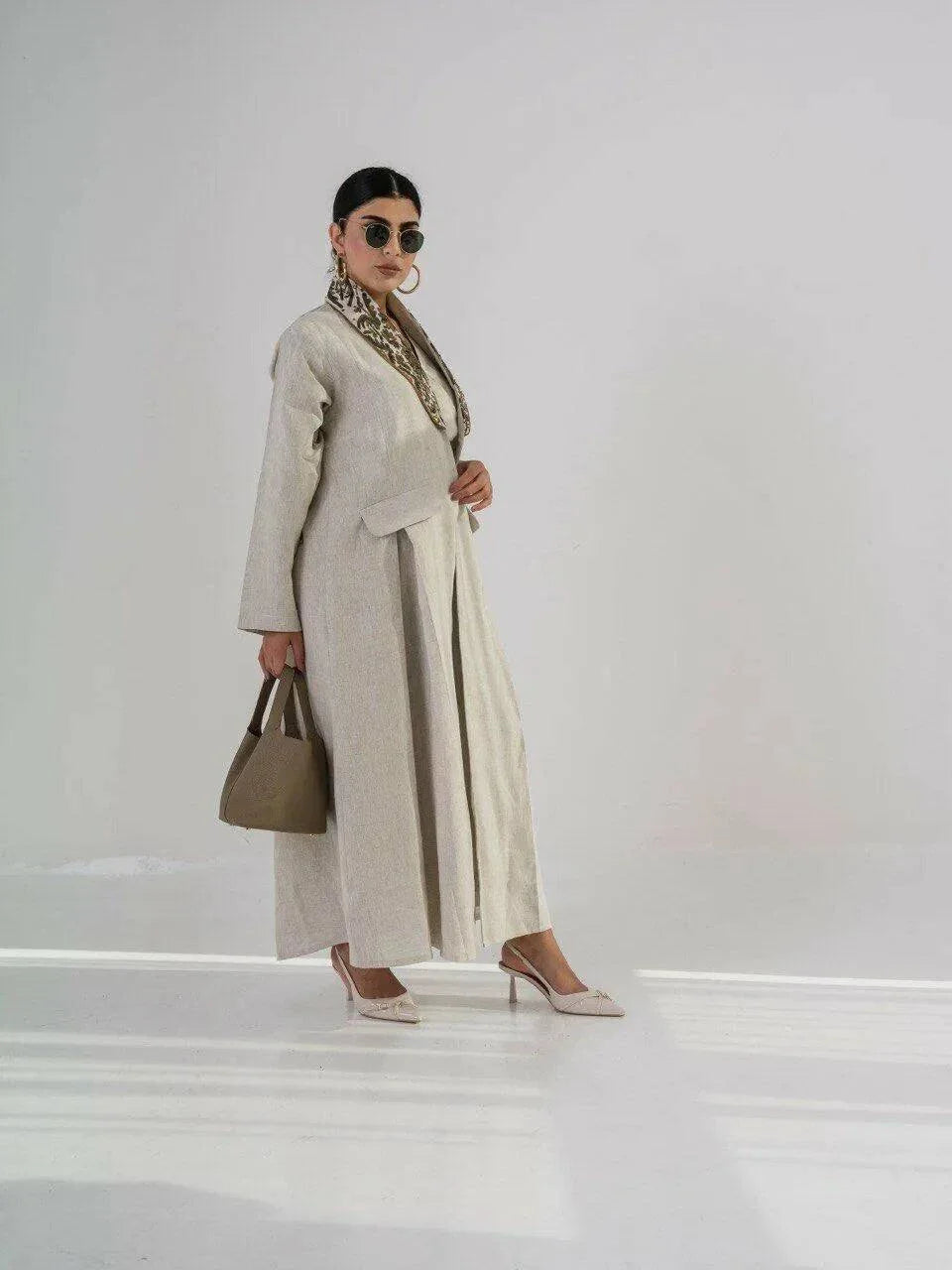 Beige blazer-style abaya made from 100% natural linen with embroidered collar and pocket pleats, styled with heels and handbag.