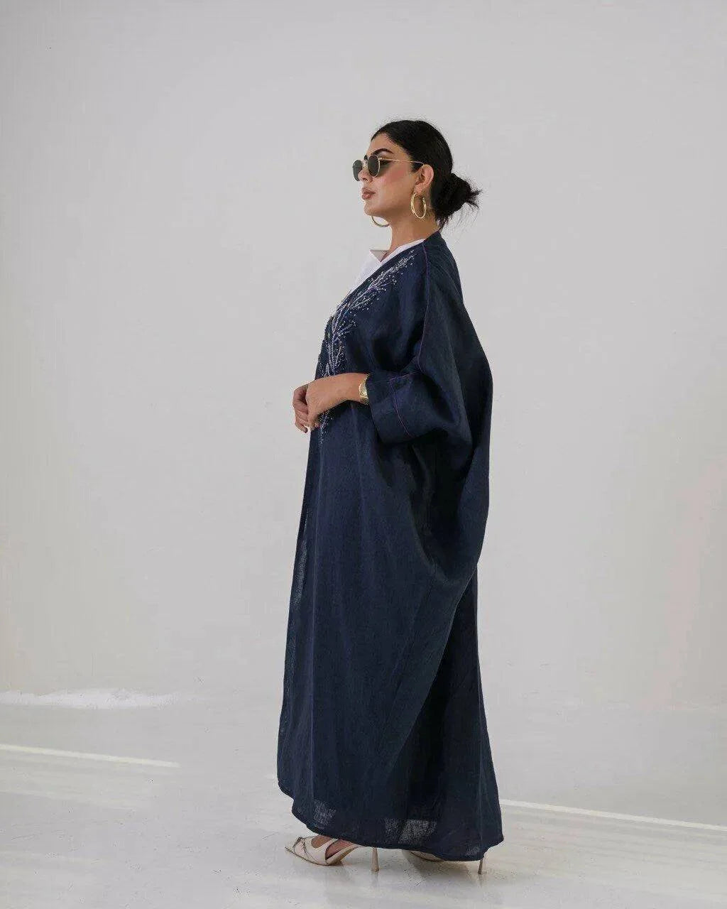Woman wearing a deep navy lightweight linen abaya with navy blue floral embroidery and wide sleeves.