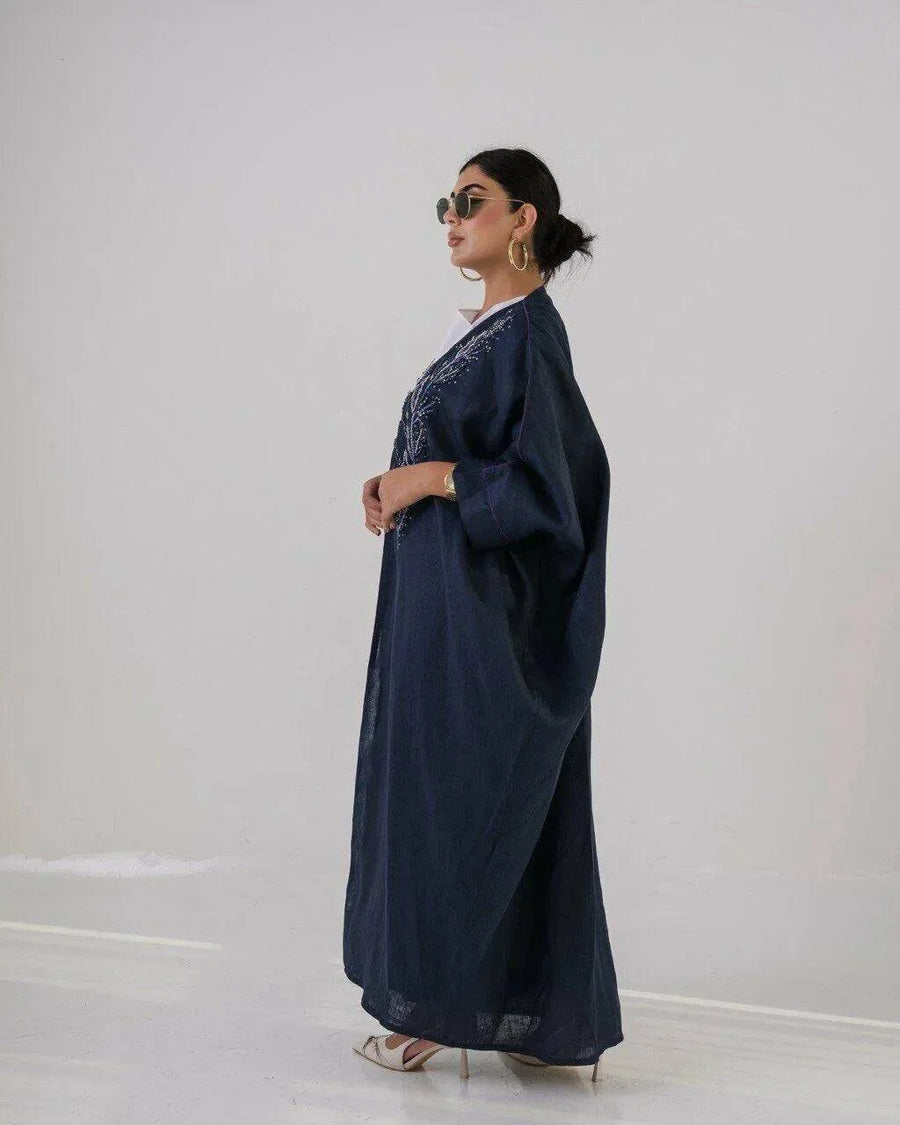 Woman wearing a deep navy lightweight linen abaya with navy blue floral embroidery and wide sleeves.