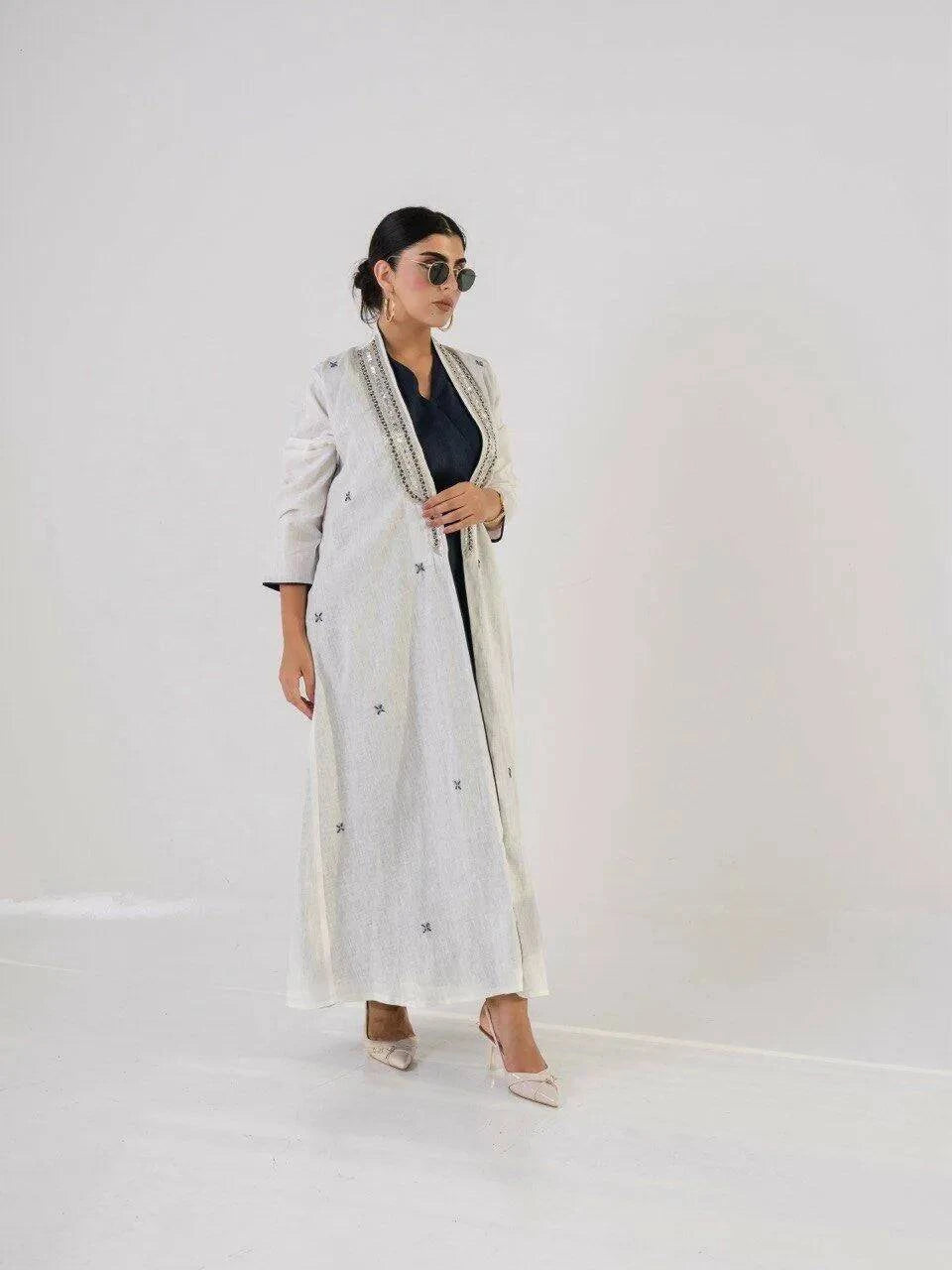 woman wearing light-colored linen abaya with intricate neckline detailing and embroidered motifs, paired with sunglasses and heels