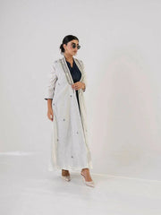 woman wearing light-colored linen abaya with intricate neckline detailing and embroidered motifs, paired with sunglasses and heels