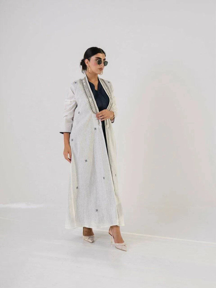 woman wearing light-colored linen abaya with intricate neckline detailing and embroidered motifs, paired with sunglasses and heels