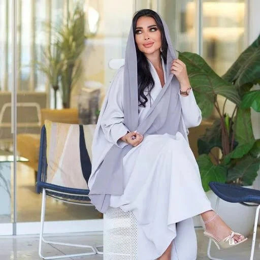 Woman wearing Perla light gray blazer abaya with hood seated indoors in modern setting