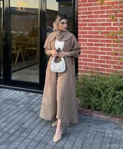 woman wearing beige abaya with relaxed silhouette holding white handbag outdoors