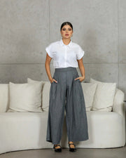 Woman wearing relaxed-fit crumpled gray linen pants with pockets and a white short-sleeve shirt standing indoors