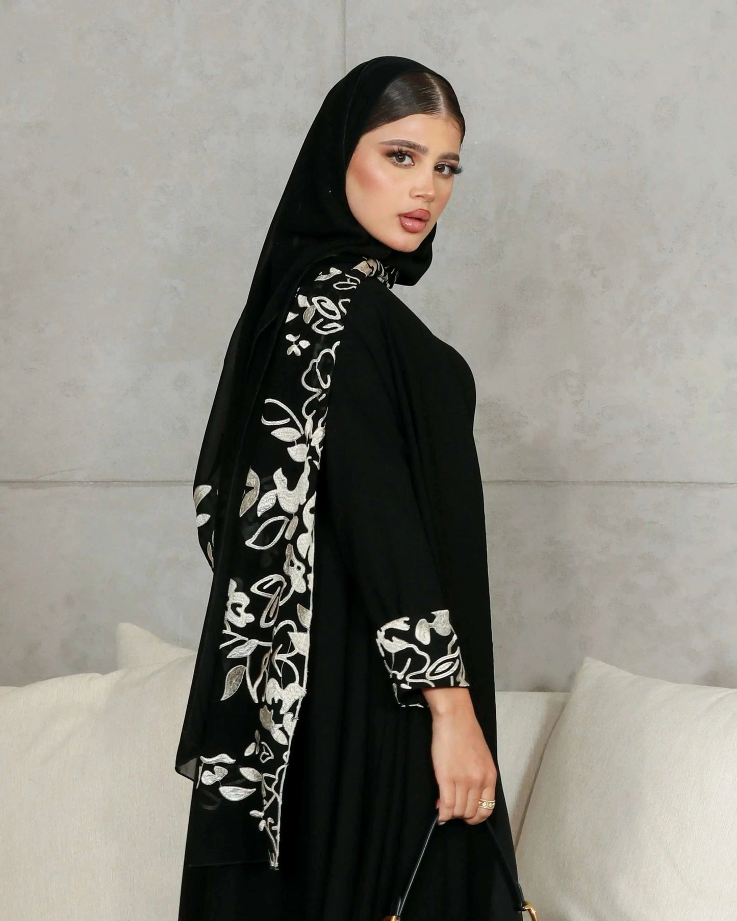 Woman wearing elegant black crepe abaya with embroidered scarf detailing on sleeves and back.