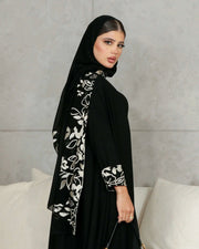 Woman wearing elegant black crepe abaya with embroidered scarf detailing on sleeves and back.
