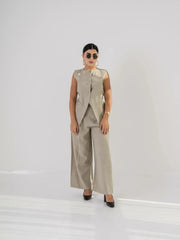 Woman wearing linen beige pants with a matching sleeveless vest and sunglasses in a minimalist setting