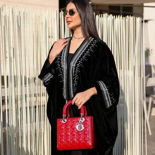 luxurious black velvet bisht abaya with silver hand embroidery worn by woman holding red handbag