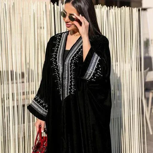 luxurious black velvet bisht abaya with silver hand embroidery worn by woman holding red handbag