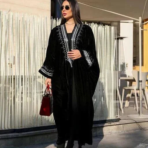 luxurious black velvet bisht abaya with silver hand embroidery worn by woman holding red handbag