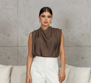 Woman wearing a stylish brown blouse crepe internet fabric paired with white pants against a gray wall background