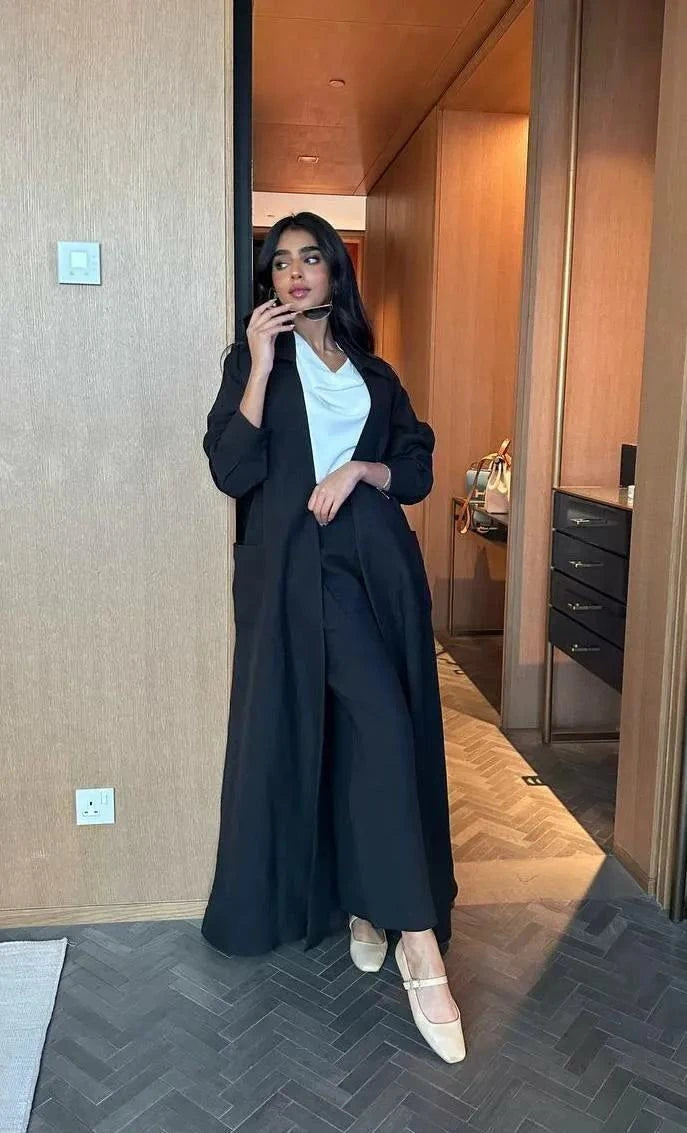 Woman wearing a relaxed black abaya with a shirt collar and pockets, styled for casual elegance.