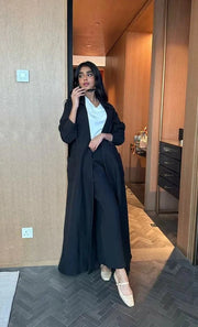 Woman wearing a relaxed black abaya with a shirt collar and pockets, styled for casual elegance.