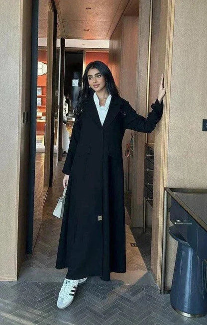 woman wearing black blazer-style abaya with button detailing on shoulders and back holding beige handbag