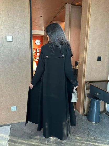 woman wearing black blazer-style abaya with button detailing on shoulders and back holding beige handbag