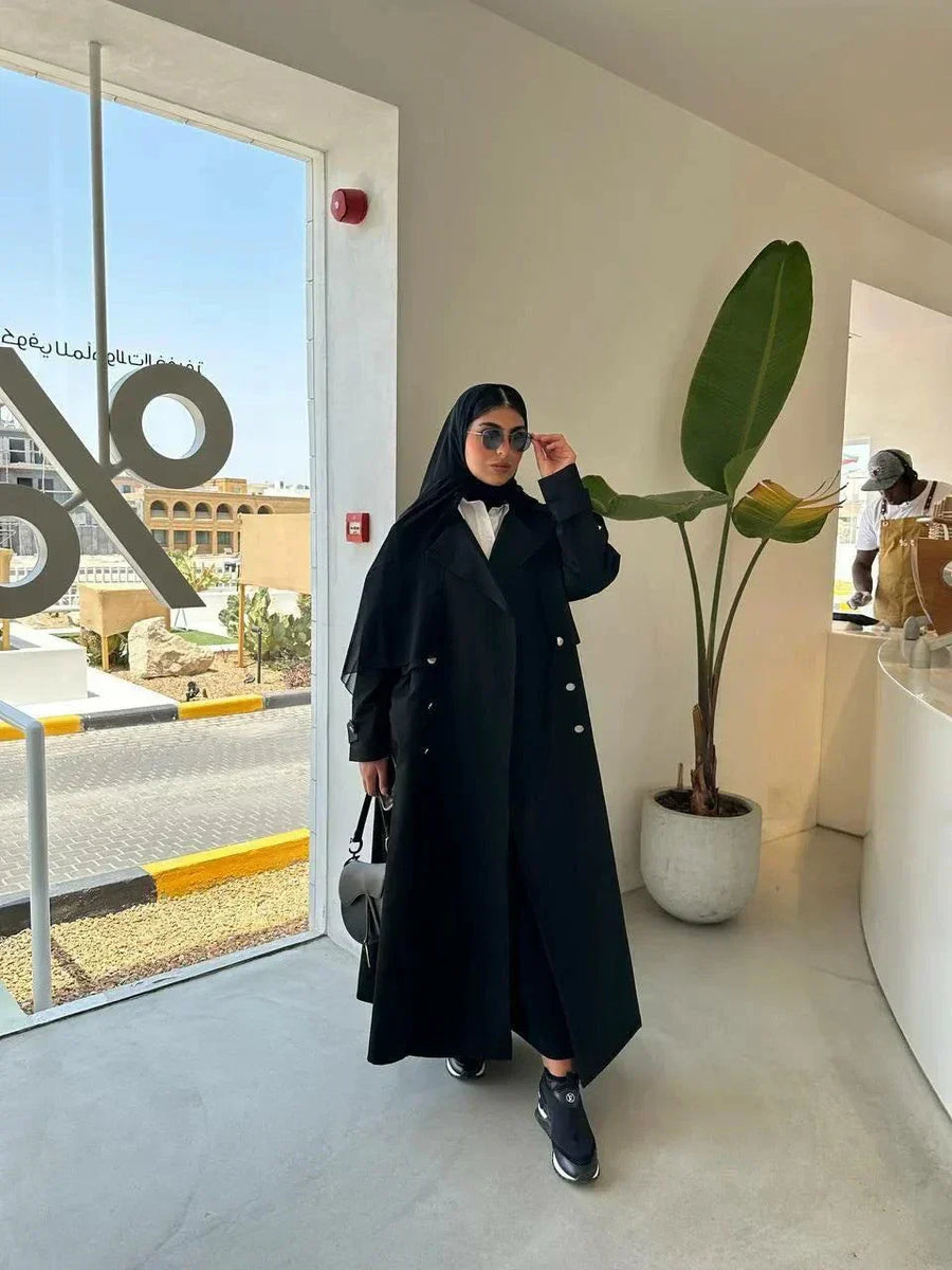 Modern black abaya with trench coat design, wide lapels, double-breasted silver buttons, and cuff details for a sophisticated look.