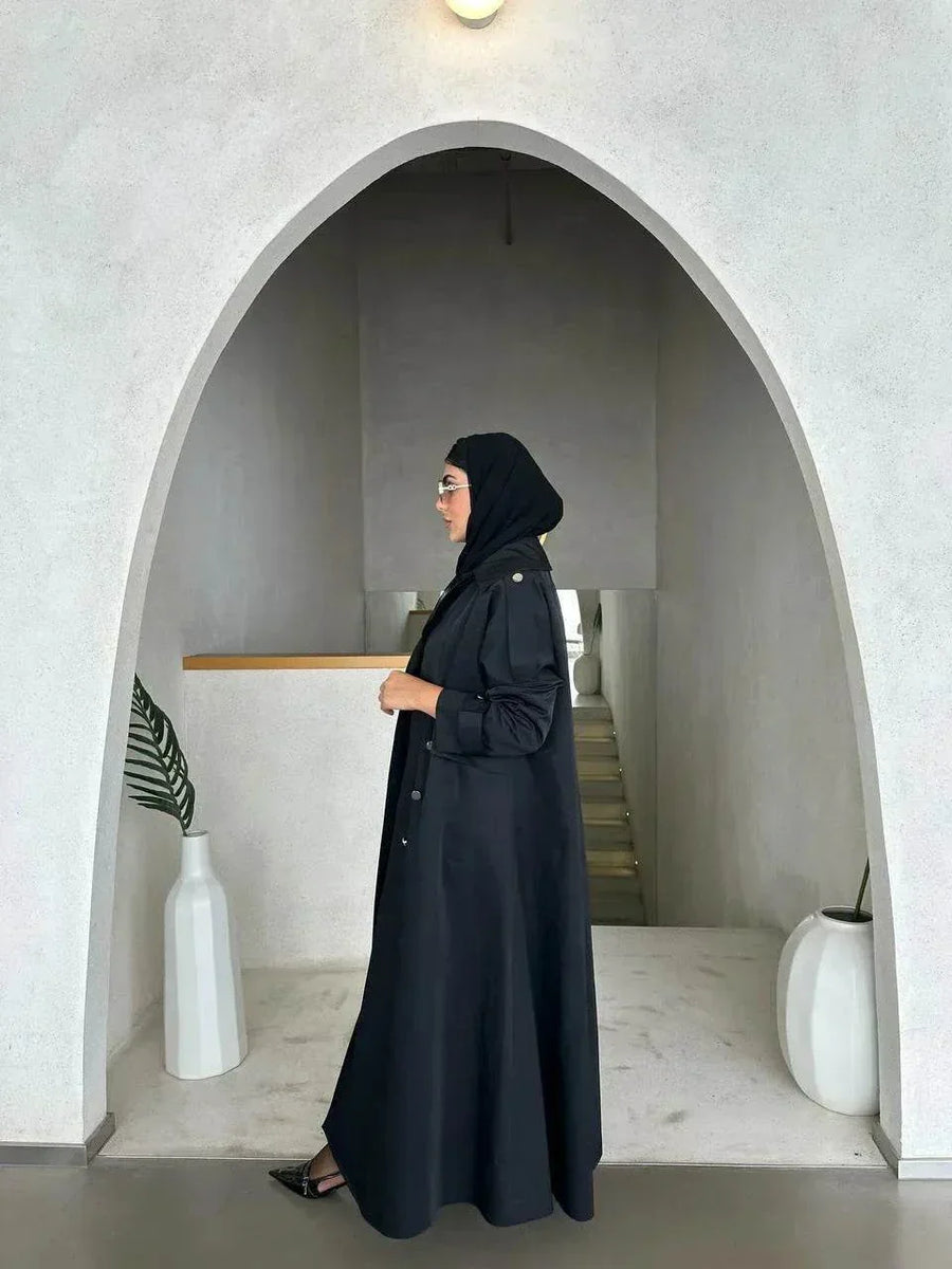 Modern black abaya with trench coat design, wide lapels, double-breasted silver buttons, and cuff details for a sophisticated look.