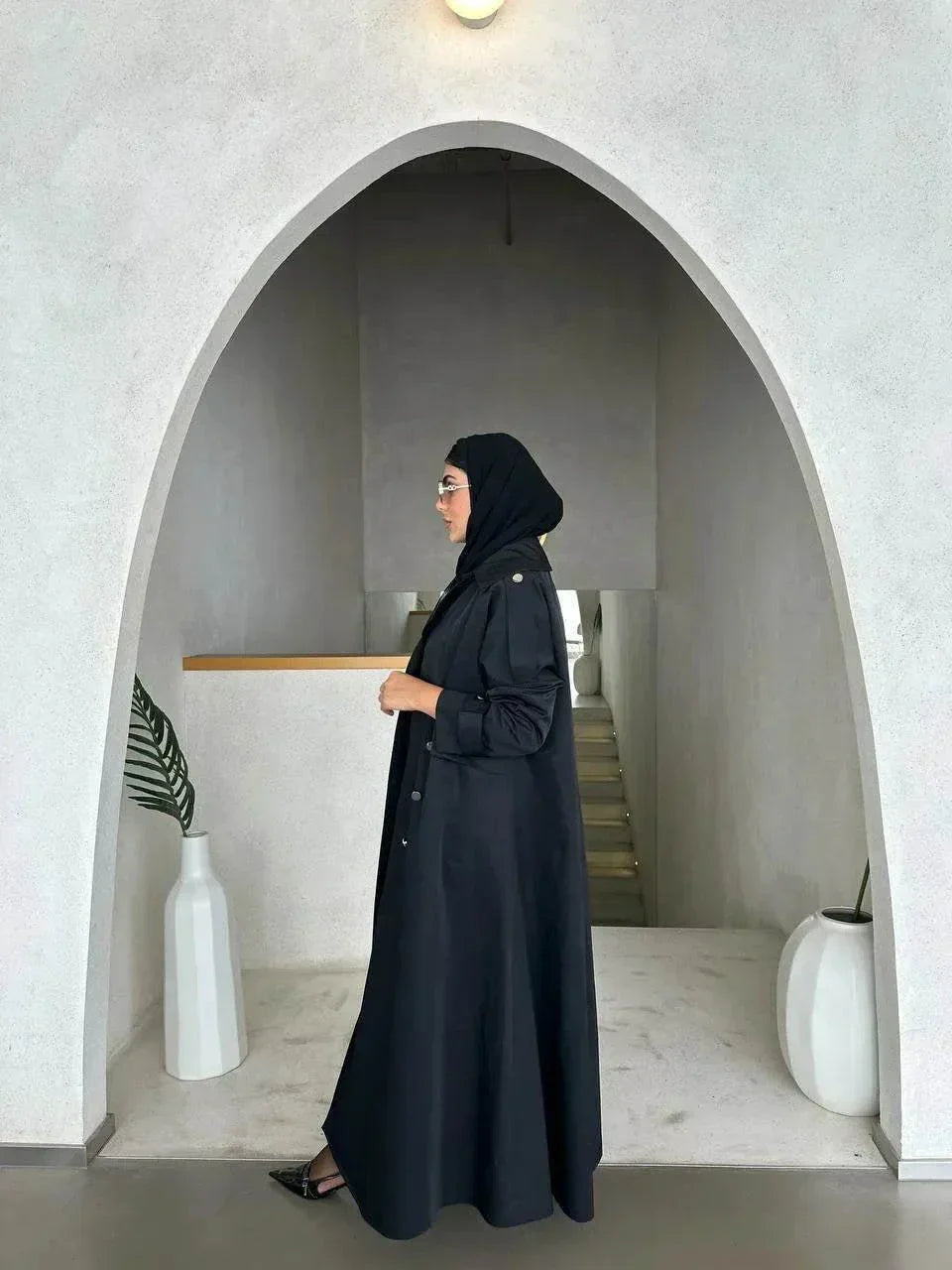 Modern black abaya with trench coat design, wide lapels, double-breasted silver buttons, and cuff details for a sophisticated look.