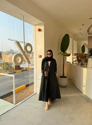 Woman wearing a sleek Noirc black blazer with subtle lined texture standing outdoors near a modern building.
