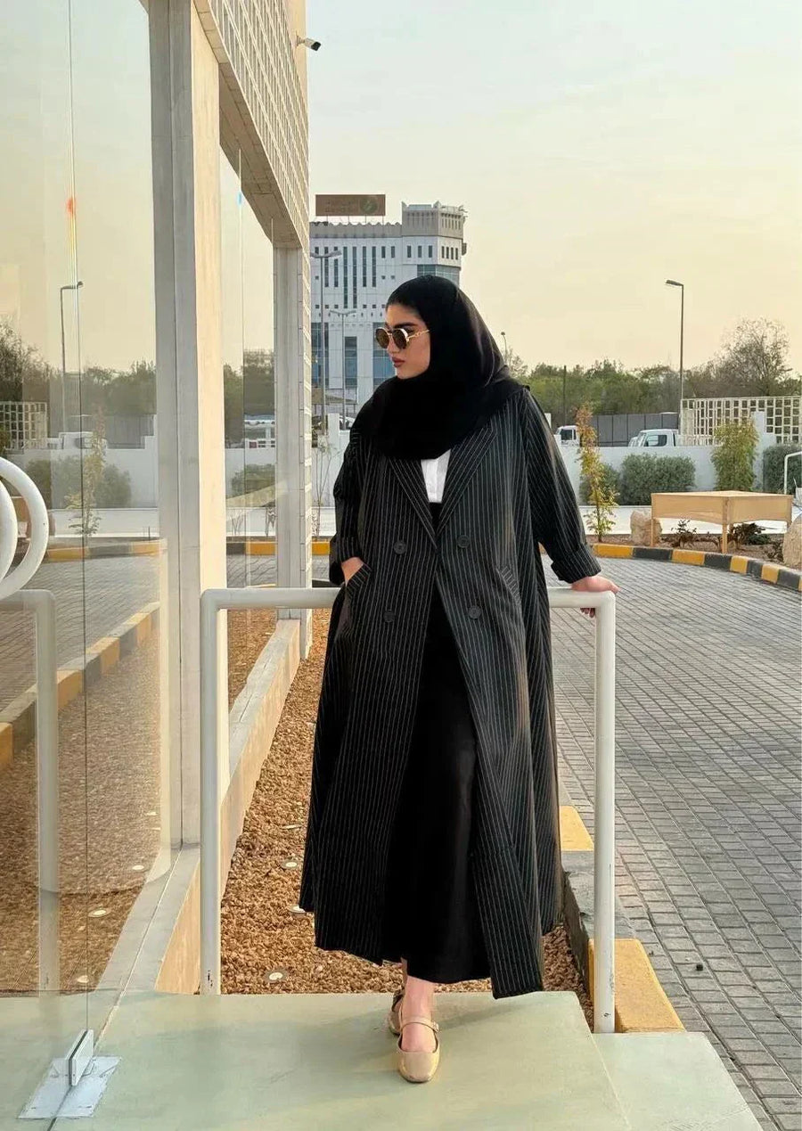 Woman wearing a sleek Noirc black blazer with subtle lined texture standing outdoors near a modern building.