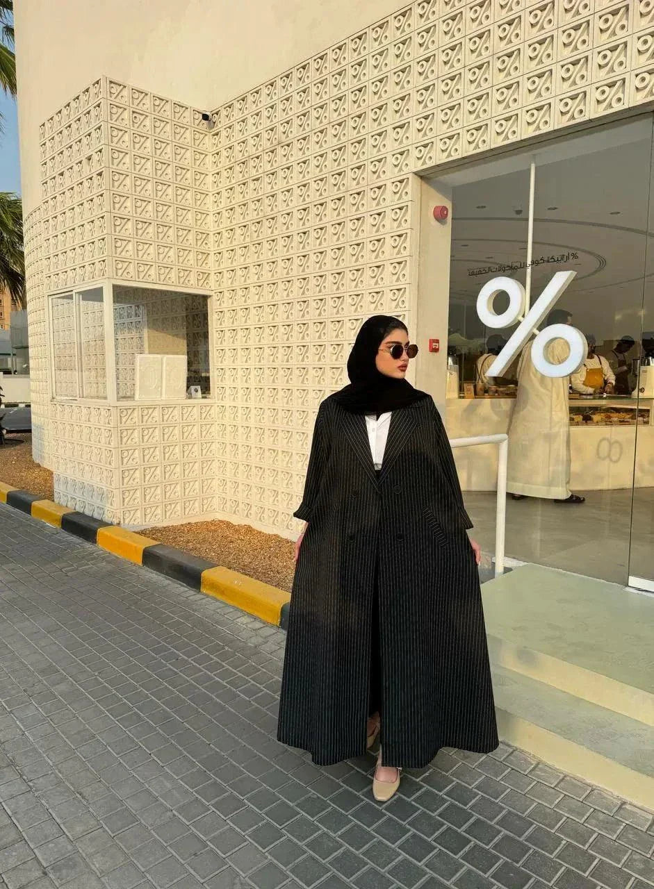 Woman wearing a sleek Noirc black blazer with subtle lined texture standing outdoors near a modern building.