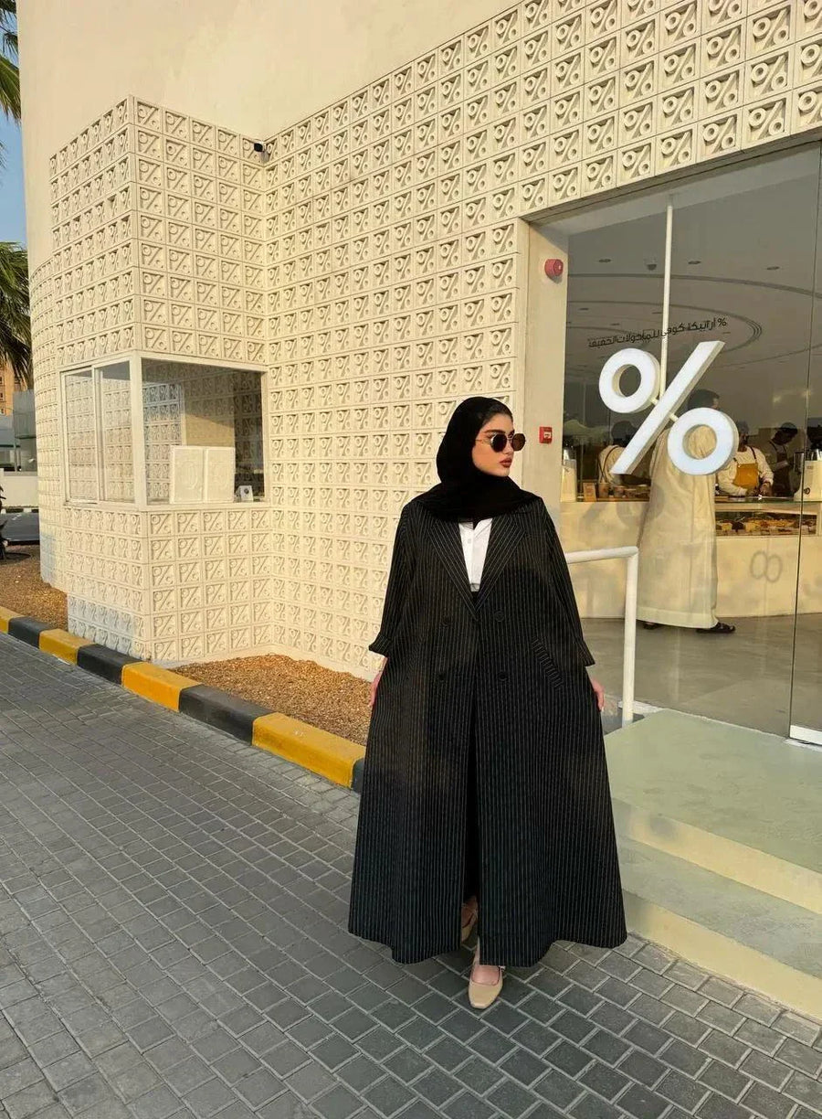 Woman wearing a sleek Noirc black blazer with subtle lined texture standing outdoors near a modern building.