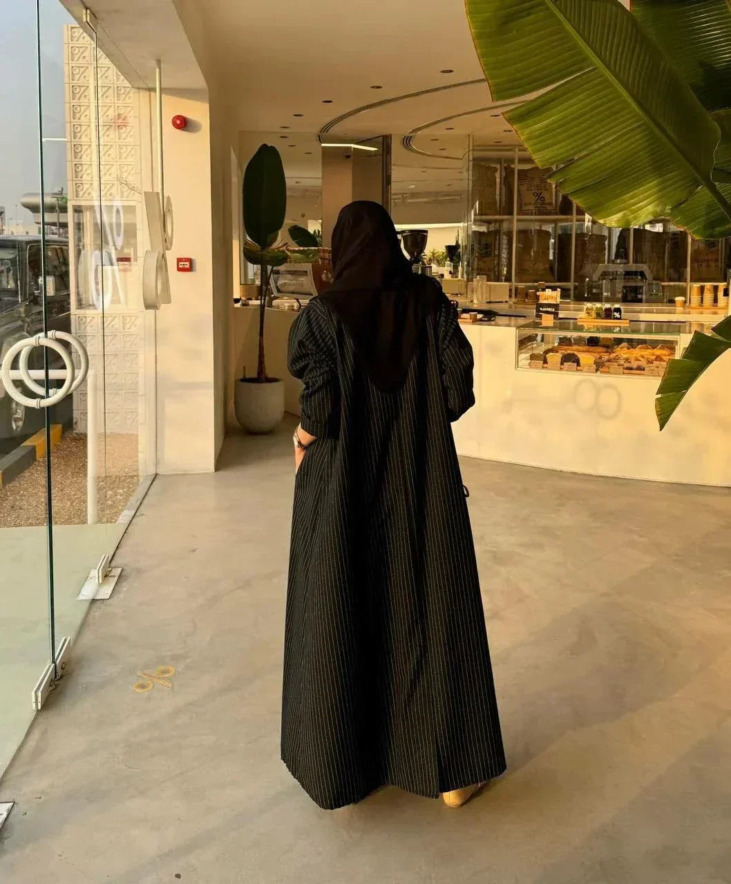 Woman wearing a sleek Noirc black blazer with subtle lined texture standing outdoors near a modern building.