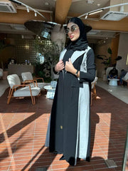 Woman wearing a modern color-block abaya in black and light grey crepe fabric with structured lapels and relaxed fit indoors
