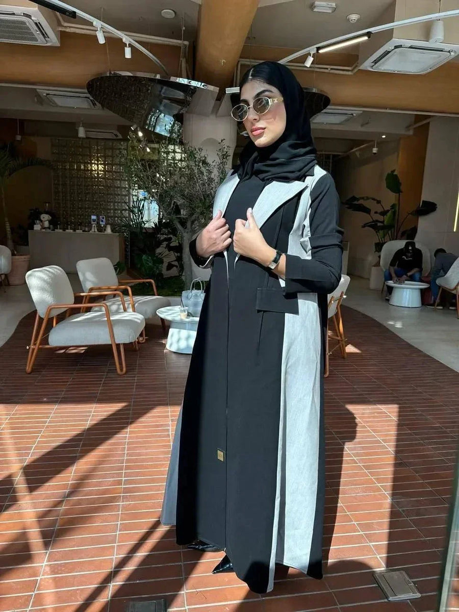 Woman wearing a modern color-block abaya in black and light grey crepe fabric with structured lapels and relaxed fit indoors