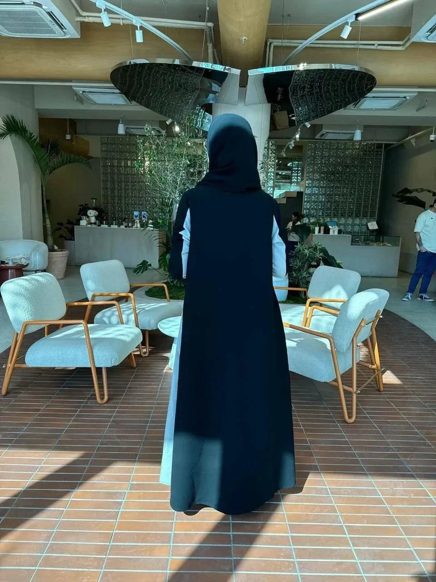 Woman wearing a modern color-block abaya in black and light grey crepe fabric with structured lapels and relaxed fit indoors