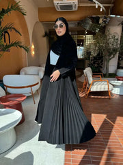 Modern black Pleera abaya with embroidered sleeves and pleated side detailing worn indoors