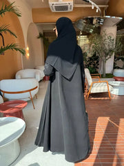 Modern black Pleera abaya with embroidered sleeves and pleated side detailing worn indoors