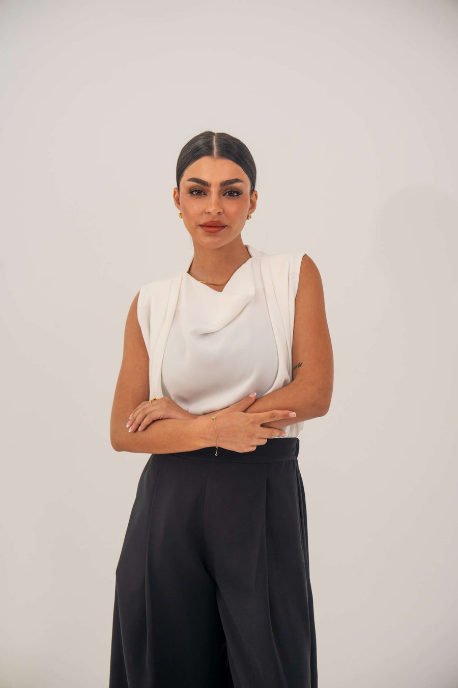 Woman wearing a sleeveless white crepe blouse with a draped neckline and black high-waisted pants