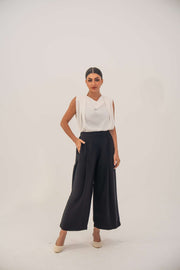 Woman wearing a sleeveless white crepe blouse with a draped neckline and black high-waisted pants