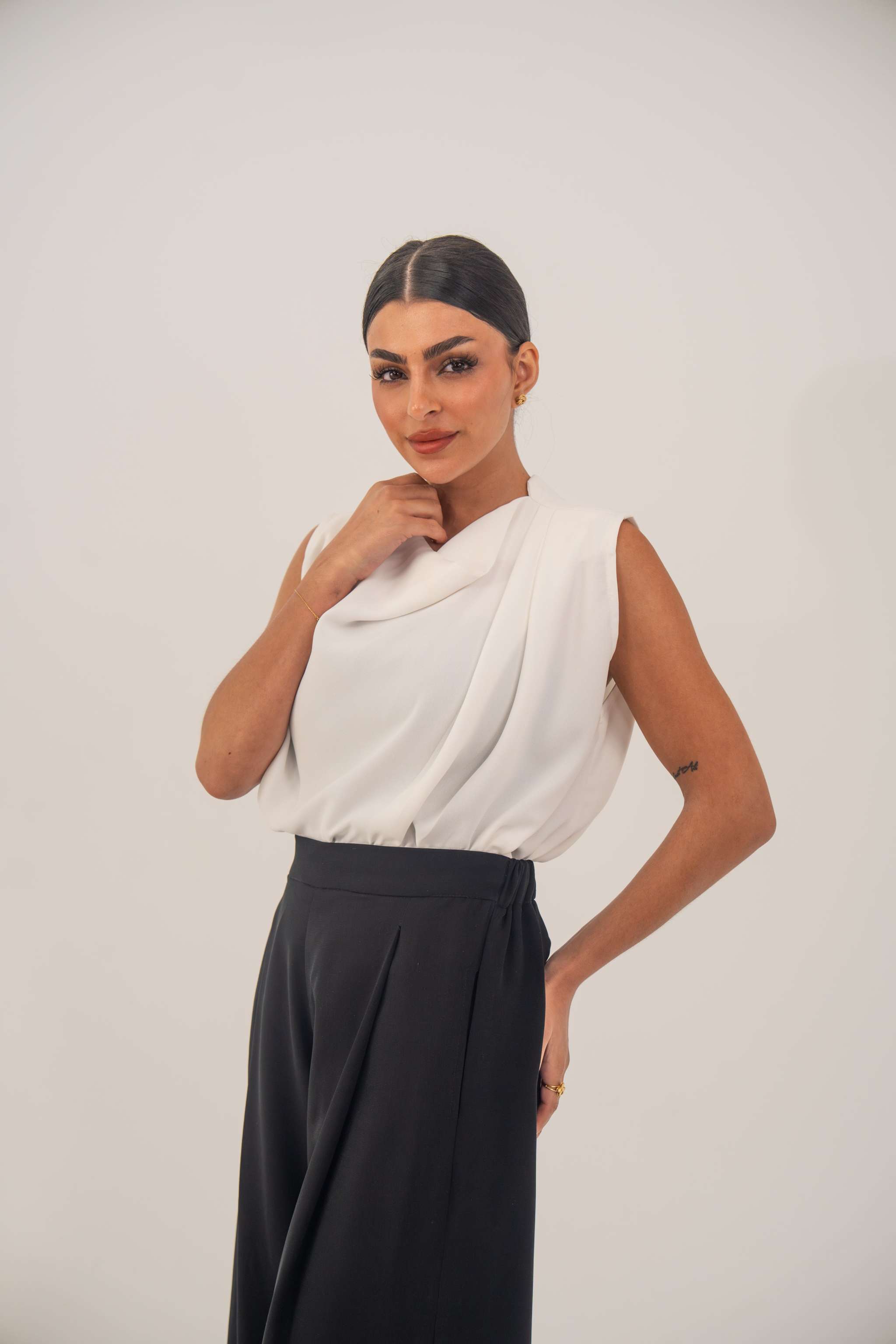 Woman wearing a sleeveless white crepe blouse with a draped neckline and black high-waisted pants
