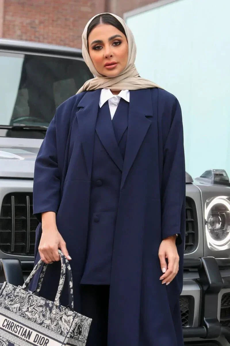 woman wearing navy blue blazer-style abaya holding patterned handbag standing in front of black SUV
