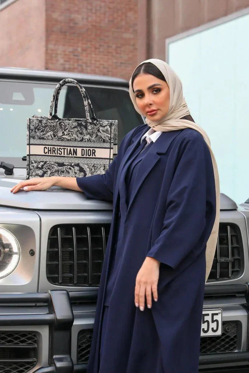 woman wearing navy blue blazer-style abaya holding patterned handbag standing in front of black SUV