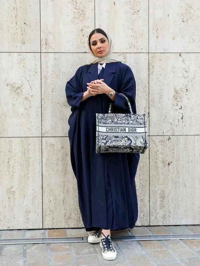 woman wearing navy blue blazer-style abaya holding patterned handbag standing in front of black SUV