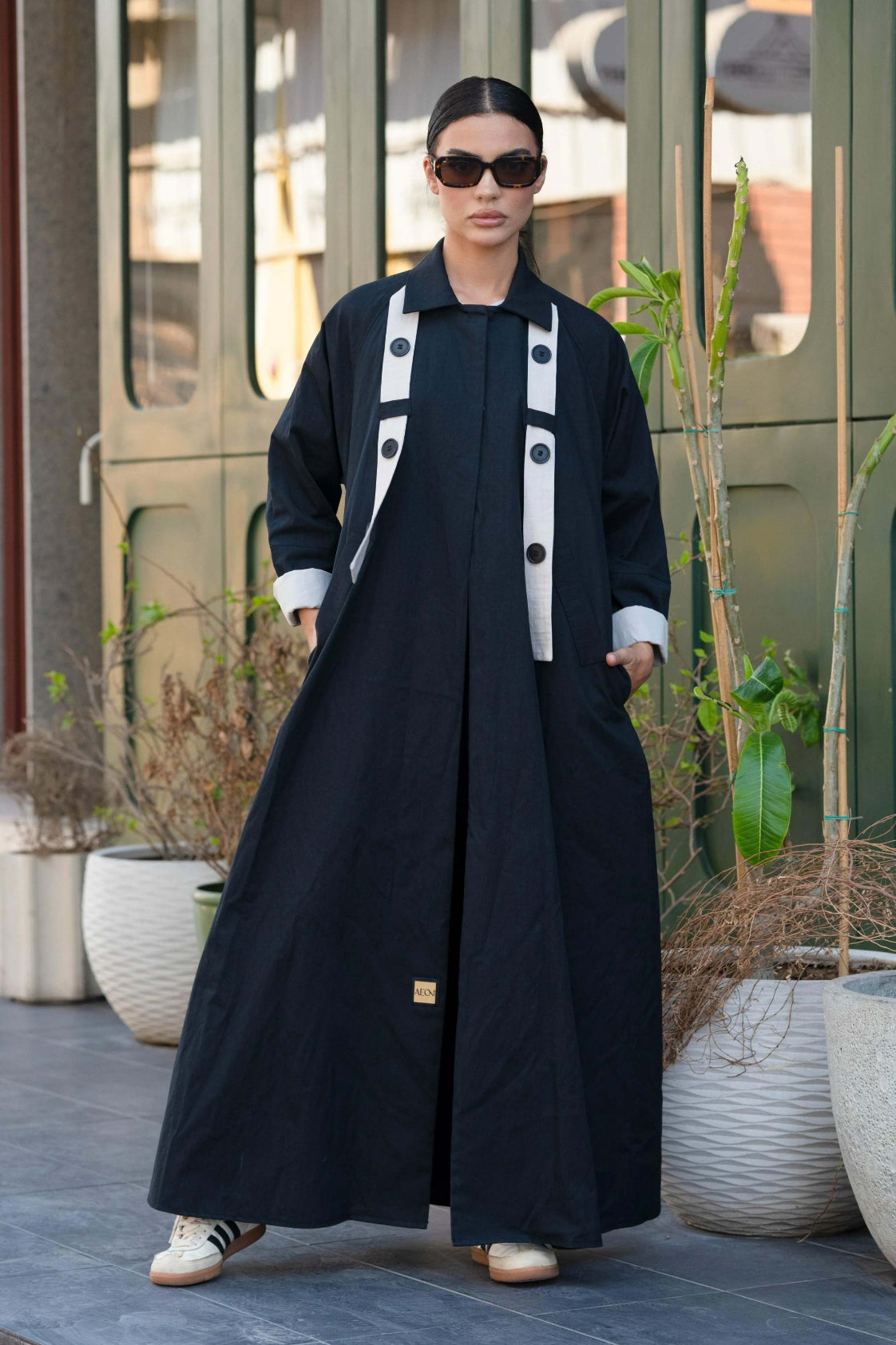 black blazer-style abaya with trench coat fabric, functional pockets, and button detail, worn with sunglasses