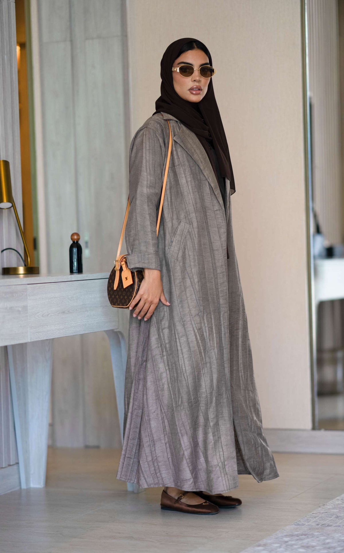woman wearing relaxed brown abaya made of crumpled linen with cappuccino shade, accessorized with sunglasses and brown handbag