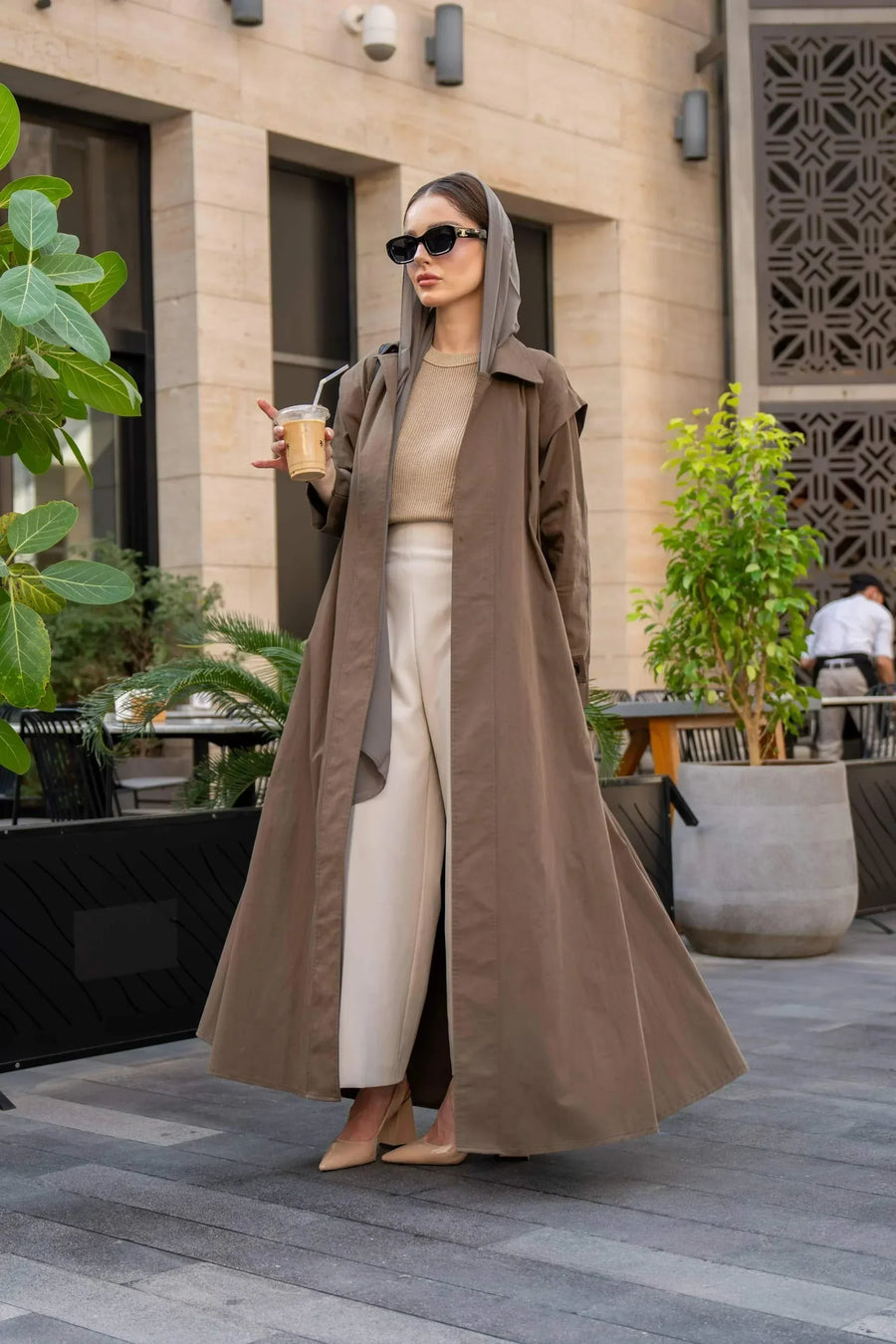 Woman Woman wearing a long coffee chino coat with tailored fit and sunglasses in an outdoor urban settingwearing a long coffee-colored chino coat with tailored fit and sunglasses in an outdoor urban setting