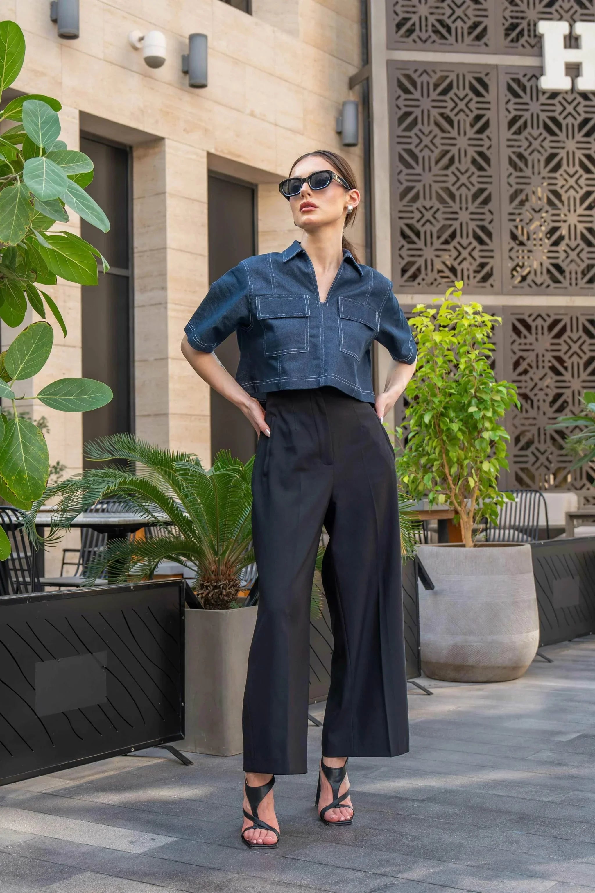 Woman wearing blue cropped blouse with front zipper and black wide-leg pants outdoors in urban setting