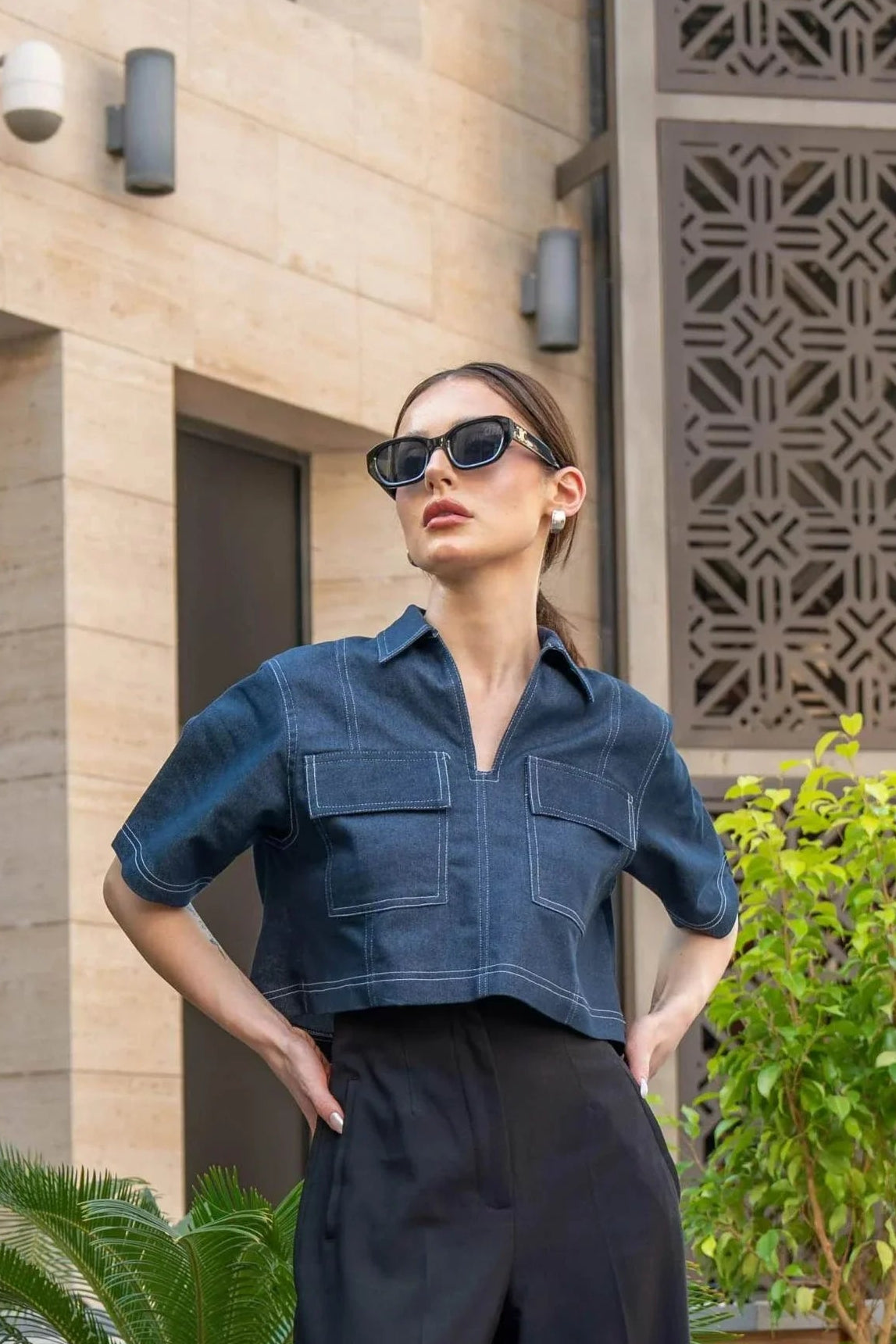 Woman wearing blue cropped blouse with front zipper and black wide-leg pants outdoors in urban setting