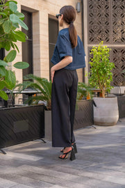 Woman wearing blue cropped blouse with front zipper and black wide-leg pants outdoors in urban setting