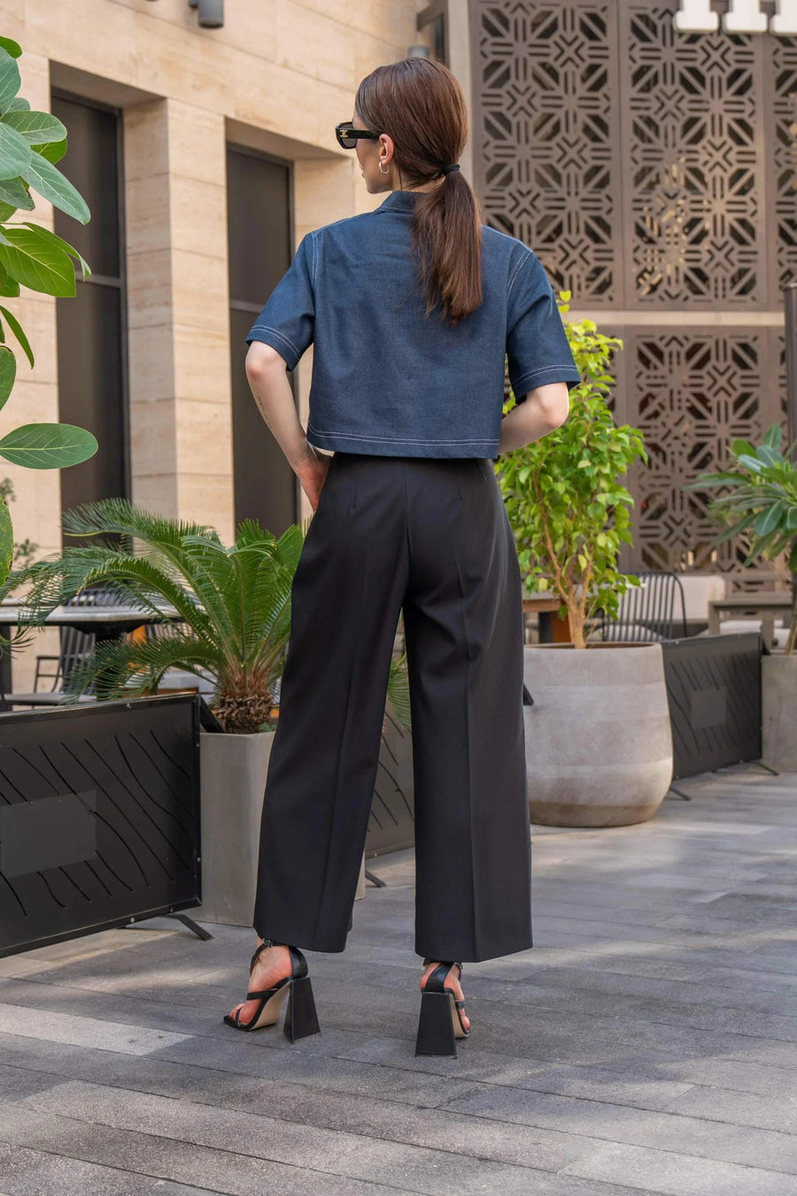 Woman wearing blue cropped blouse with front zipper and black wide-leg pants outdoors in urban setting