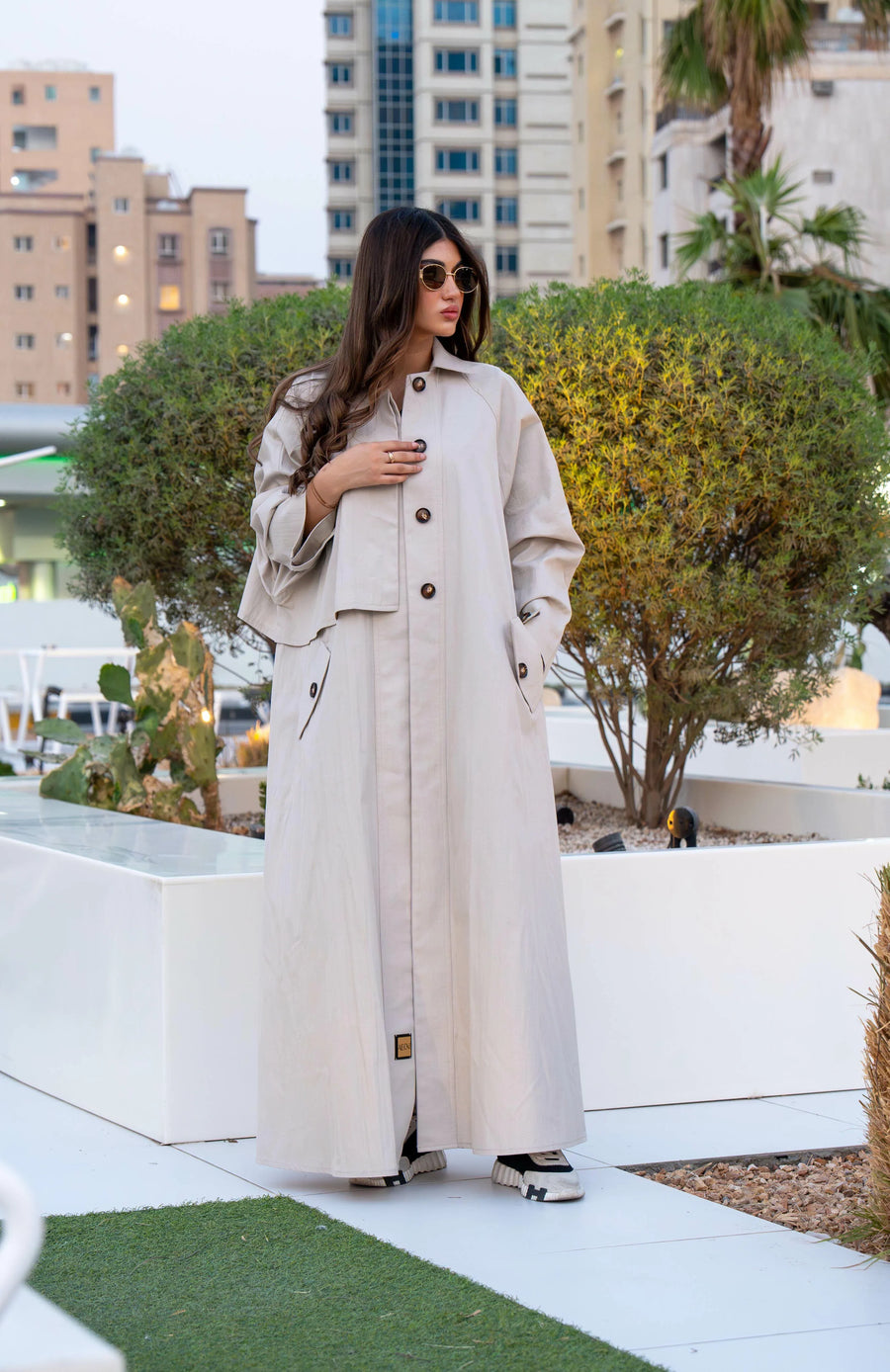 Woman wearing beige Sandline free-size trench coat with front buttons and flap pockets outdoors